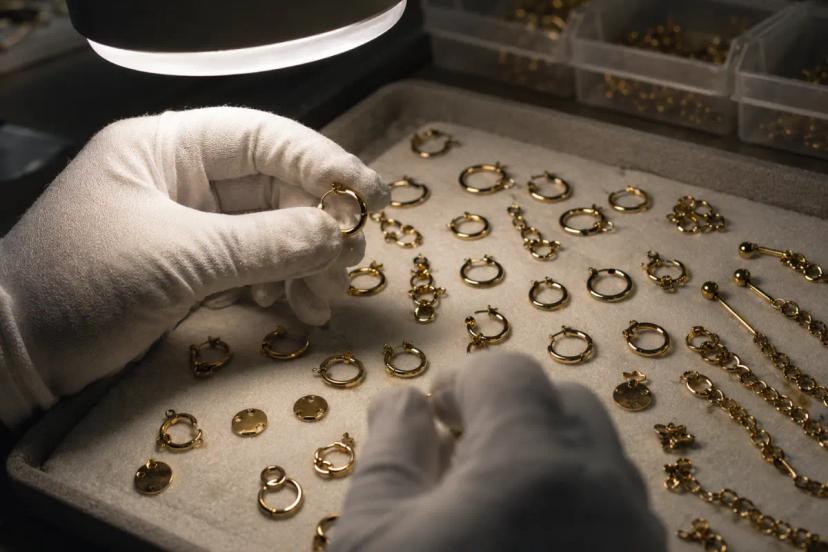 Gloved worker inspecting gold-look PVD stainless steel jewelry samples during batch QC