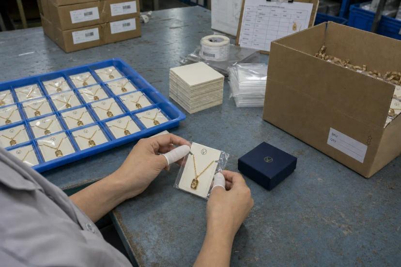 Worker checking approved jewelry packaging samples, box consistency and barcode labels before repeat production
