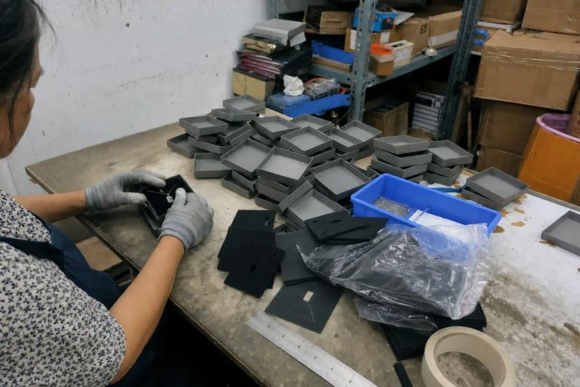Jewelry packaging worker assembling necklace inserts and box components at a production workstation