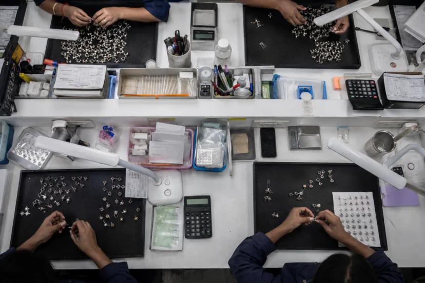 Top-down jewelry workshop where workers sort stone-set components and inspect pieces during production