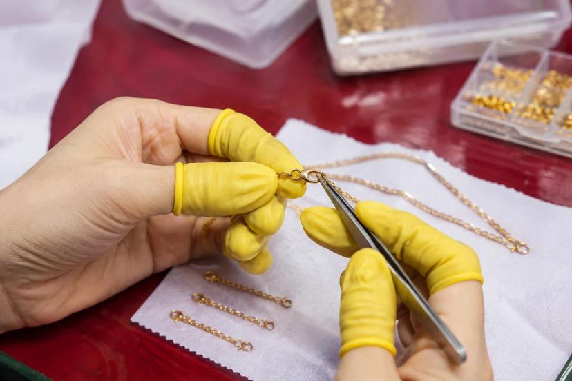 Jewelry construction quality control inspecting a gold chain clasp and jump ring with tweezers
